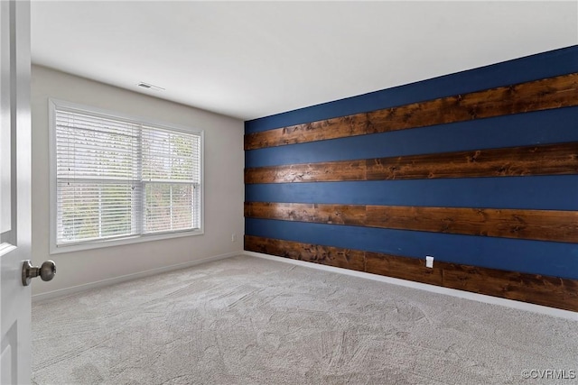 spare room featuring baseboards, visible vents, carpet floors, and wood walls