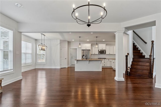unfurnished living room with a notable chandelier, dark wood finished floors, recessed lighting, stairway, and decorative columns