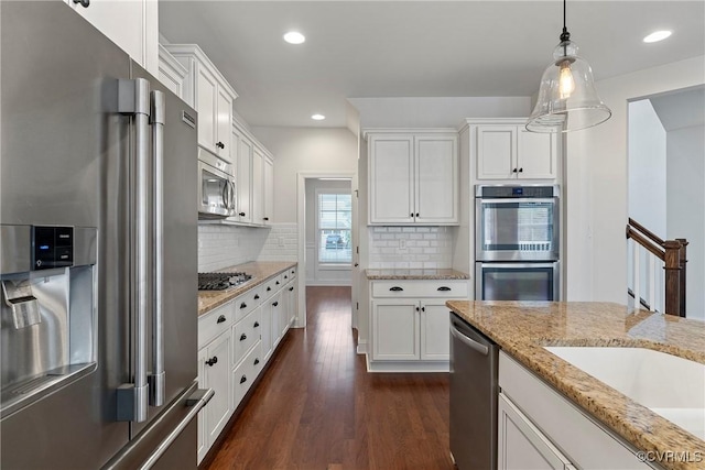 kitchen with tasteful backsplash, dark wood finished floors, pendant lighting, appliances with stainless steel finishes, and white cabinetry