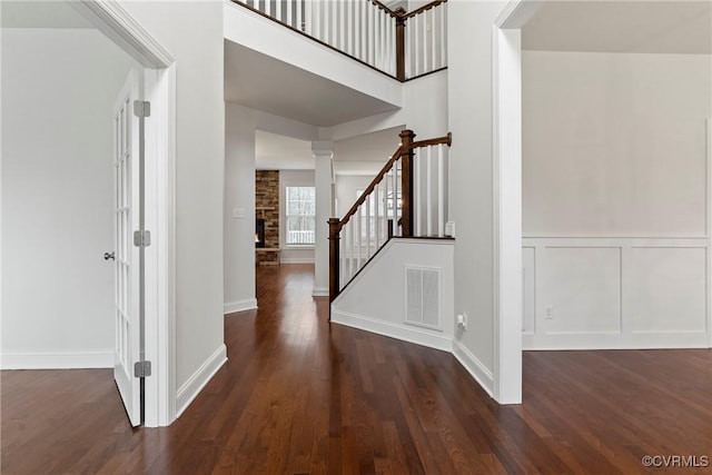 foyer entrance featuring visible vents, wood finished floors, stairway, a large fireplace, and a decorative wall