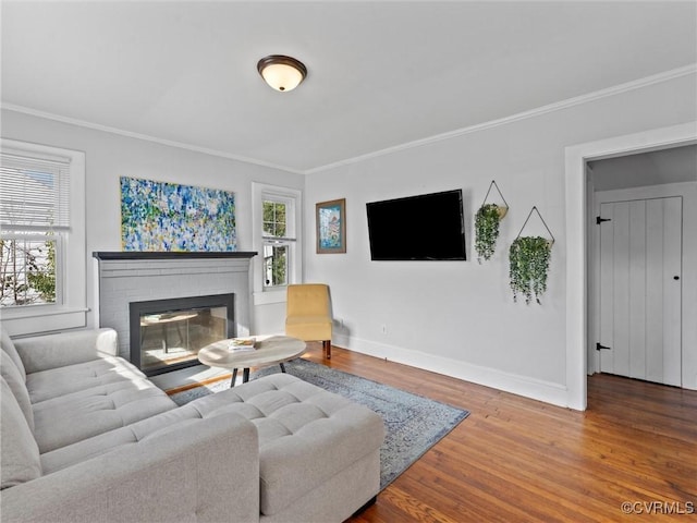 living room with baseboards, wood finished floors, a brick fireplace, and ornamental molding