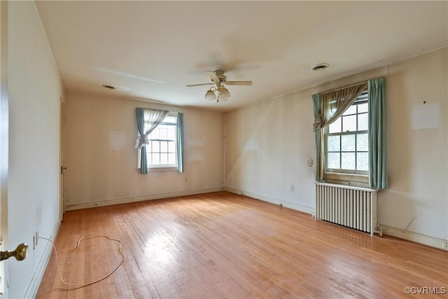 spare room featuring visible vents, radiator, baseboards, ceiling fan, and wood-type flooring