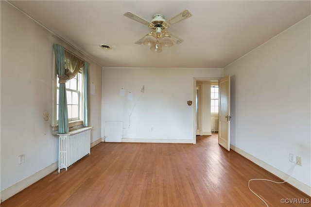 empty room with radiator, wood finished floors, visible vents, and ceiling fan