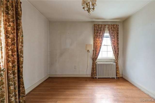 empty room featuring radiator, wood finished floors, and baseboards