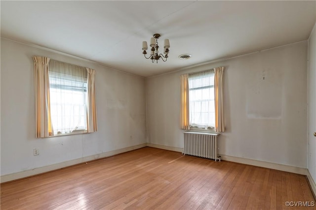 unfurnished room with visible vents, radiator, an inviting chandelier, and light wood finished floors