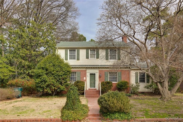 view of front of property with brick siding, a chimney, and a front yard