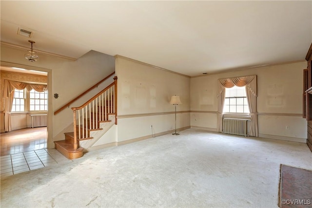 unfurnished living room featuring a wealth of natural light, radiator, and stairs