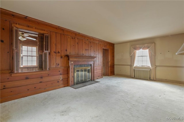 unfurnished living room featuring a fireplace with flush hearth, carpet floors, radiator, wooden walls, and baseboards