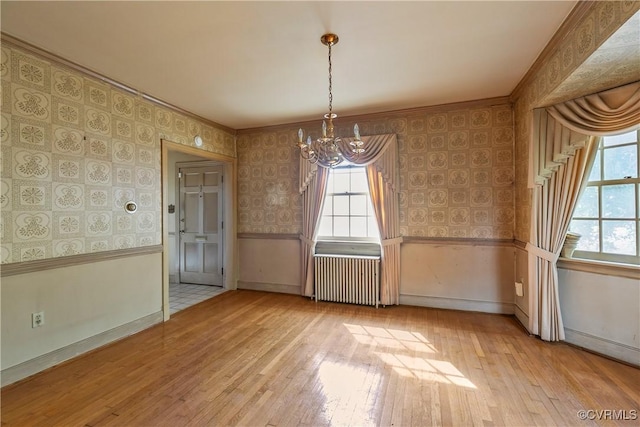 unfurnished dining area featuring hardwood / wood-style floors, wainscoting, radiator heating unit, and wallpapered walls