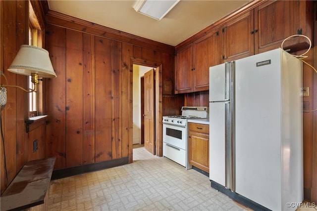 kitchen with brown cabinets, white appliances, wood walls, light countertops, and light floors