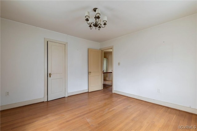 unfurnished room featuring a notable chandelier, baseboards, and light wood finished floors