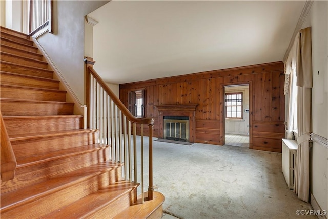 stairs with wooden walls, carpet flooring, and a fireplace with flush hearth