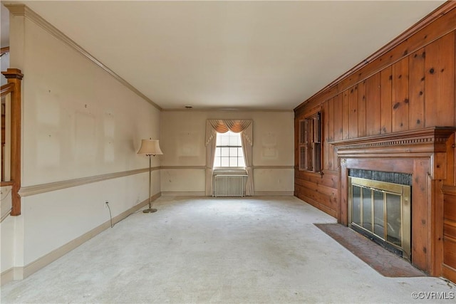 unfurnished living room with crown molding, a fireplace with flush hearth, radiator heating unit, carpet flooring, and wainscoting