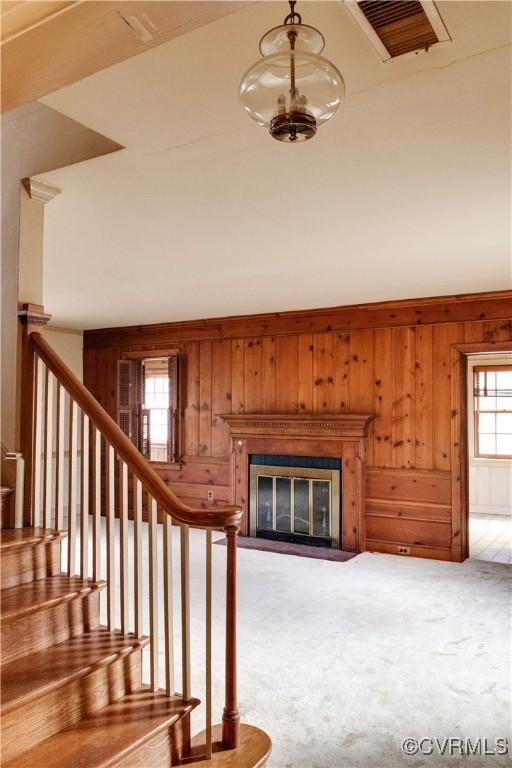 stairway with a glass covered fireplace, carpet, visible vents, and wood walls