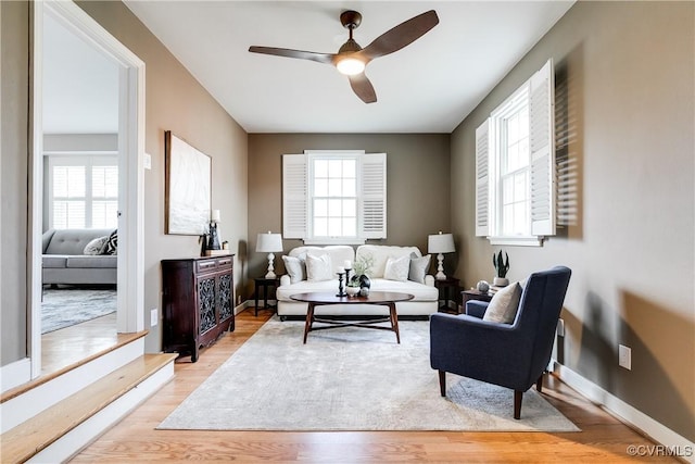 living area with light wood-style flooring, baseboards, and ceiling fan