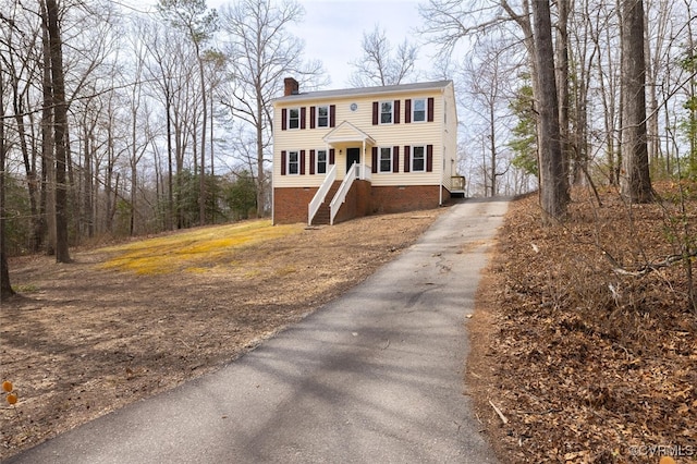 view of front of home featuring crawl space, a chimney, and driveway