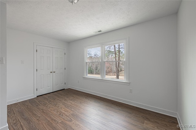 unfurnished bedroom featuring visible vents, dark wood-type flooring, a textured ceiling, a closet, and baseboards