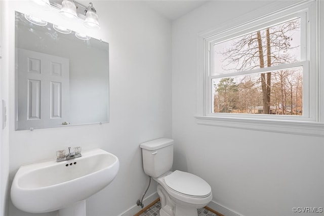 half bathroom with toilet, baseboards, and a sink