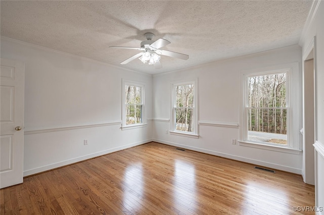 empty room with wood finished floors, visible vents, and ornamental molding