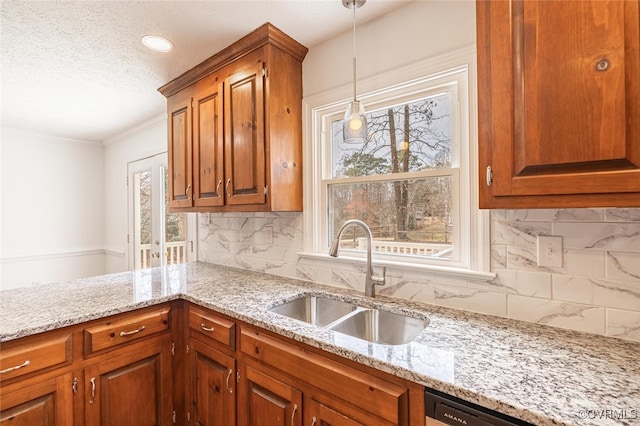 kitchen with hanging light fixtures, dishwashing machine, light stone counters, and a sink