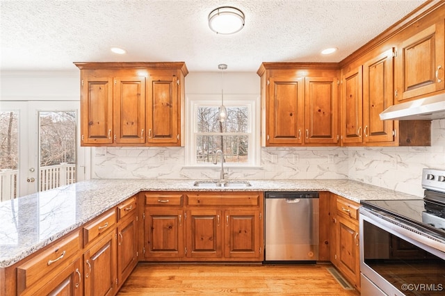 kitchen featuring under cabinet range hood, stainless steel appliances, light stone counters, and a sink