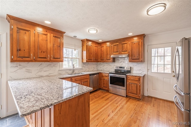 kitchen featuring brown cabinetry, a peninsula, a sink, stainless steel appliances, and under cabinet range hood