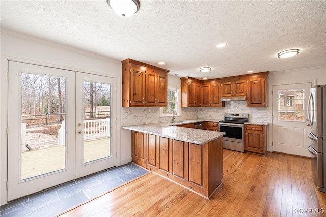 kitchen with brown cabinets, a sink, under cabinet range hood, stainless steel appliances, and a peninsula