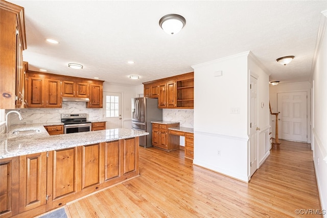 kitchen featuring a sink, under cabinet range hood, appliances with stainless steel finishes, a peninsula, and brown cabinetry