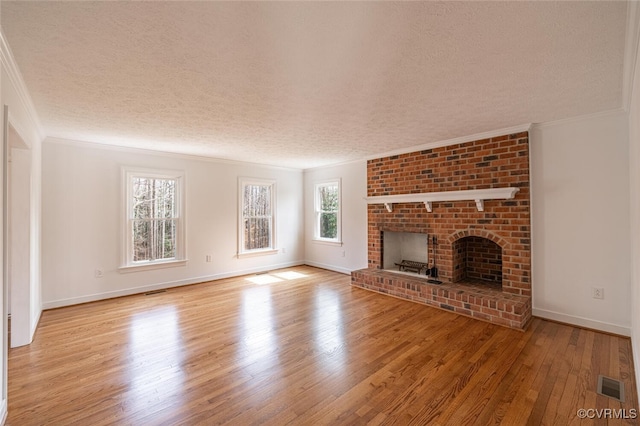 unfurnished living room with visible vents, ornamental molding, a textured ceiling, wood finished floors, and a brick fireplace