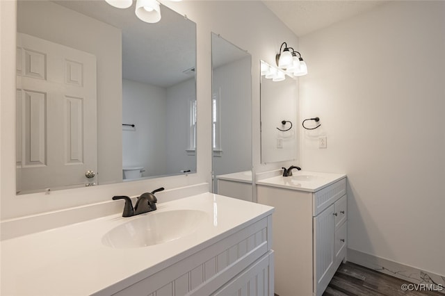 bathroom with a sink, toilet, two vanities, and wood finished floors