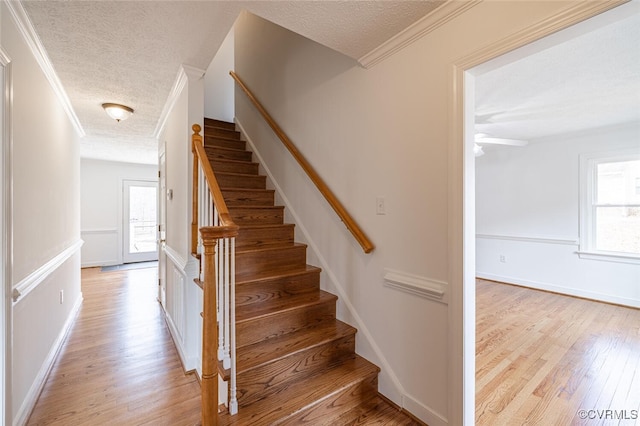 stairs featuring crown molding, plenty of natural light, and wood finished floors