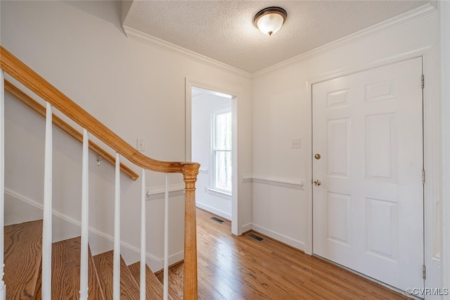 entrance foyer with visible vents, light wood-style flooring, ornamental molding, stairs, and a textured ceiling