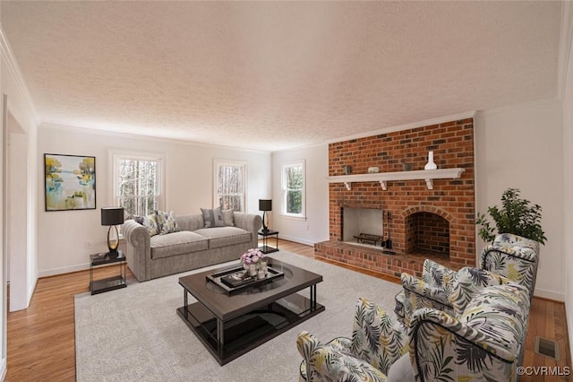 living room with visible vents, a textured ceiling, wood finished floors, crown molding, and a brick fireplace