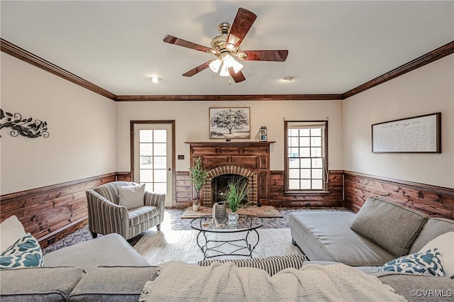 living area featuring a brick fireplace, plenty of natural light, wood walls, and wainscoting