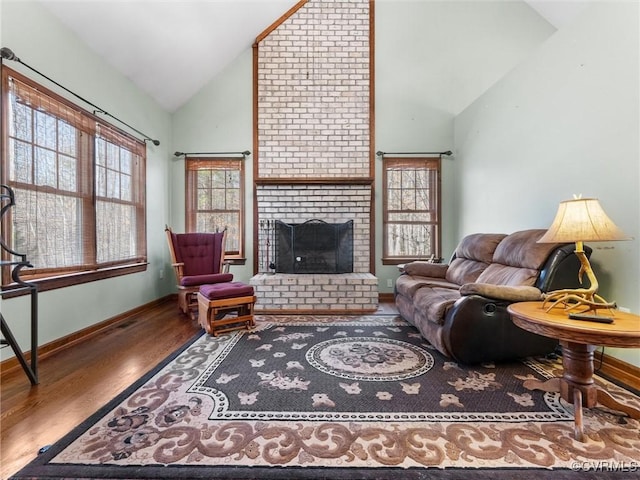 living area featuring baseboards, high vaulted ceiling, a brick fireplace, and wood finished floors