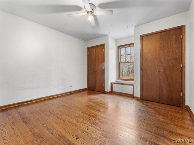 unfurnished bedroom featuring baseboards, a ceiling fan, wood finished floors, and multiple closets