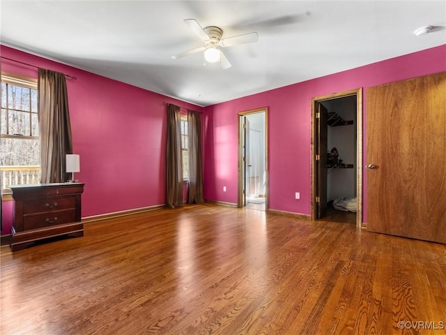 unfurnished bedroom with ceiling fan, a closet, wood finished floors, and a spacious closet