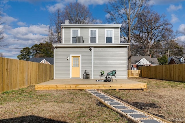 rear view of property featuring a wooden deck, a lawn, a fenced backyard, and a chimney