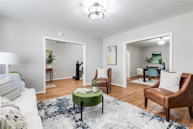 living area with light wood-style flooring, stairs, and baseboards