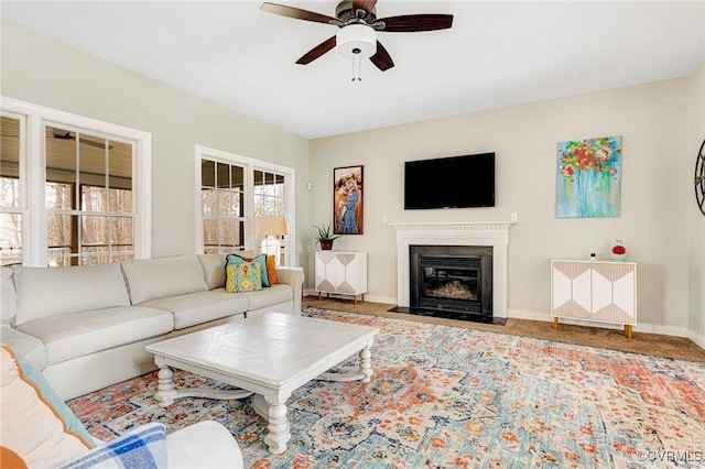 living area featuring baseboards, a fireplace with flush hearth, carpet floors, and ceiling fan