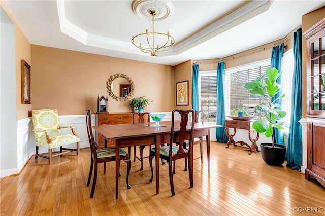 dining space with light wood-type flooring, a raised ceiling, a notable chandelier, and crown molding