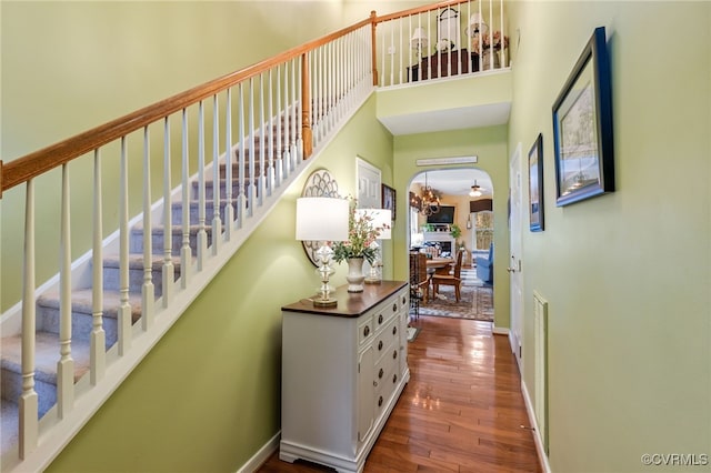 hall featuring baseboards, stairs, a high ceiling, hardwood / wood-style flooring, and a notable chandelier