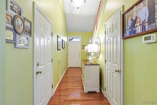 hall with visible vents, baseboards, lofted ceiling, and light wood finished floors