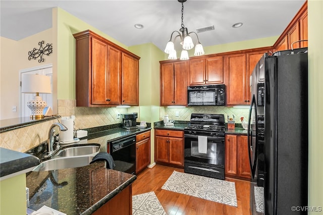 kitchen featuring light wood finished floors, tasteful backsplash, a notable chandelier, black appliances, and a sink