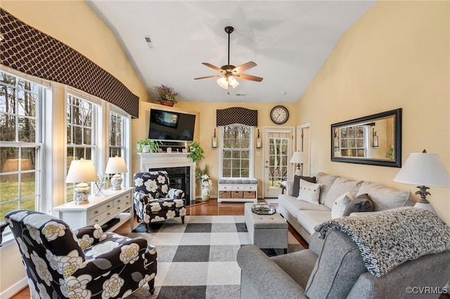 living area featuring a premium fireplace, visible vents, ceiling fan, and vaulted ceiling