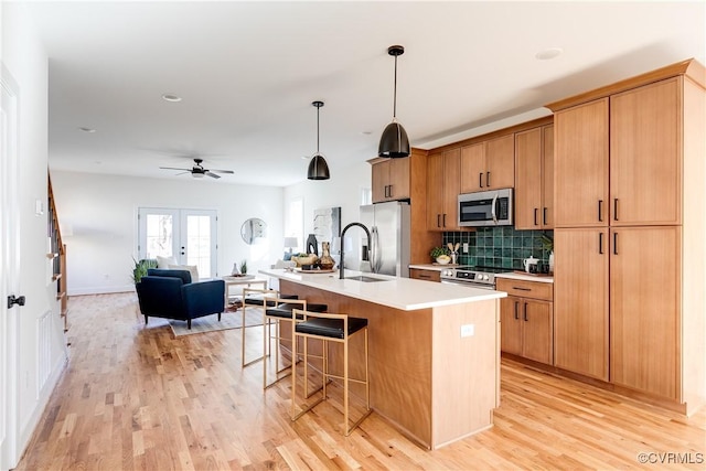 kitchen featuring a kitchen island with sink, a sink, appliances with stainless steel finishes, a kitchen bar, and light wood-type flooring