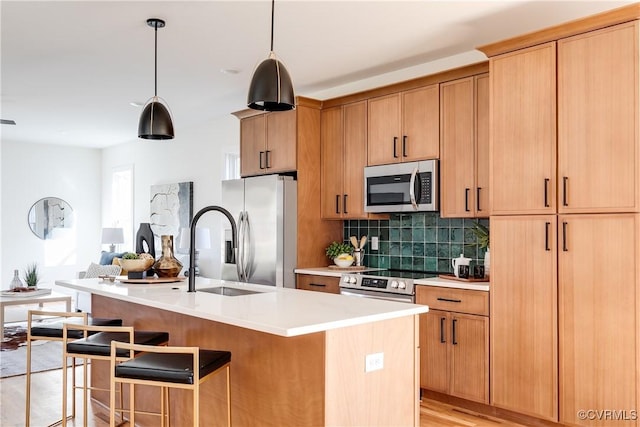 kitchen with tasteful backsplash, light countertops, appliances with stainless steel finishes, a kitchen breakfast bar, and a sink