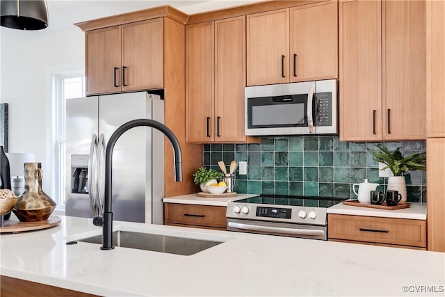 kitchen featuring tasteful backsplash, light stone countertops, appliances with stainless steel finishes, brown cabinetry, and a sink