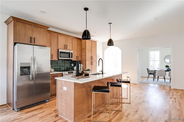 kitchen with backsplash, an island with sink, light countertops, stainless steel appliances, and a sink