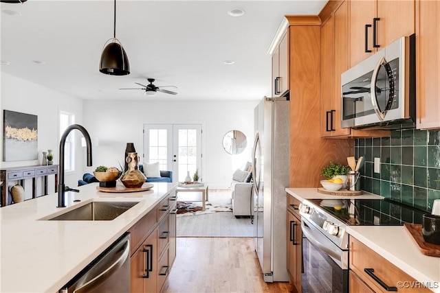 kitchen with open floor plan, decorative backsplash, light wood-style floors, stainless steel appliances, and a sink